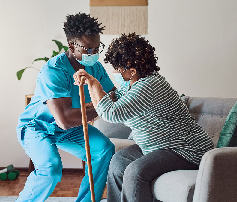 Nurse assisting elderly woman to stand with a cane