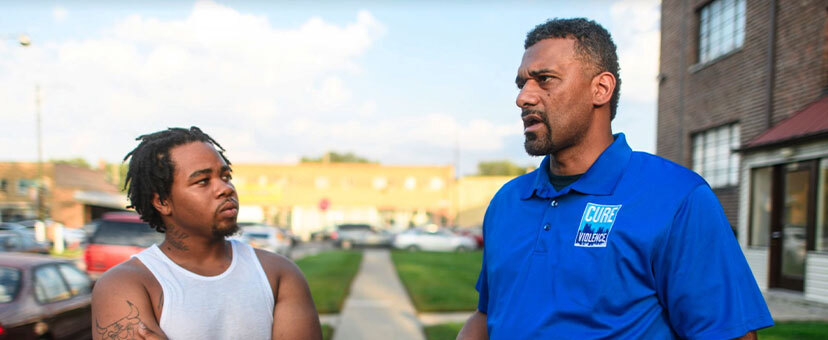 Two men speaking one is wearing a Cure Violence shirt